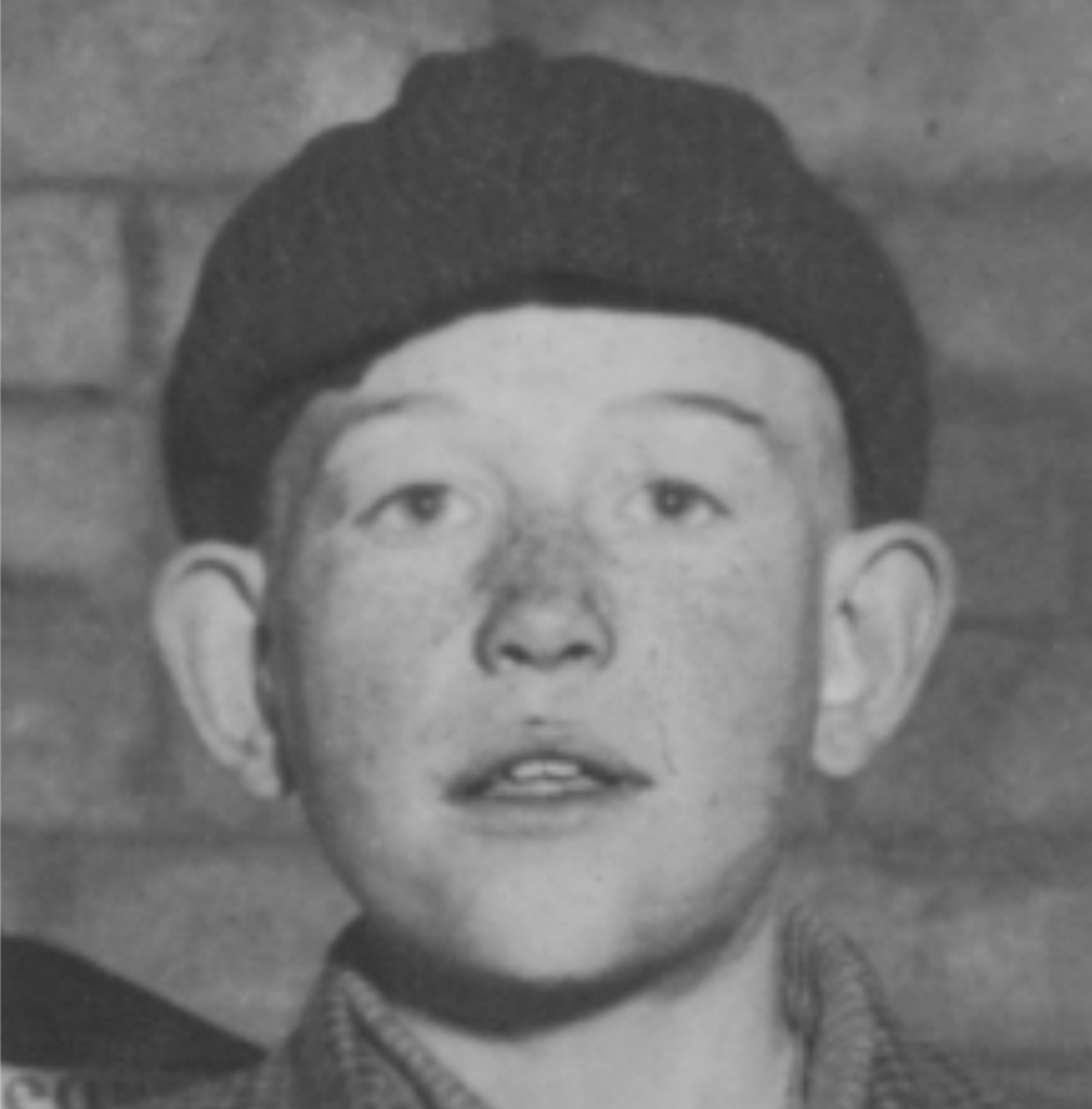 Photograph of a 15-year-old boy in 1910, wearing some type of cloth cap. Looking directly at the camera, eyes open, protruding ears, perhaps freckled. 